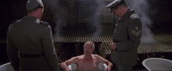 Movie still from “Richard III” (1995), directed by Richard Loncraine – A man sitting in a chair in front of two men; Wide shot, High angle