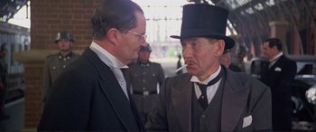 Movie still from “Richard III” (1995), directed by Richard Loncraine – A man in a top hat is talking to another man; Close Up shot, Over the shoulder angle