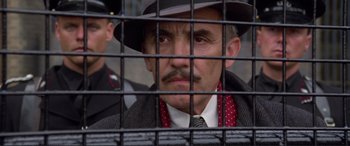 Movie still from “Richard III” (1995), directed by Richard Loncraine – A man in a hat and tie behind a fence; Close Up shot, Low angle