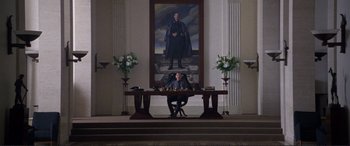 Movie still from “Richard III” (1995), directed by Richard Loncraine – A man sitting at a table in front of a painting; Wide shot, Low angle