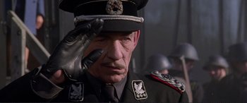 Movie still from “Richard III” (1995), directed by Richard Loncraine – An older man in a uniform saluting with his hand raised; Close Up shot, Low angle
