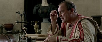 Movie still from “Risen” (2016), directed by Kevin Reynolds – A man sitting at a table in front of a statue; Close Up shot, Over the shoulder angle