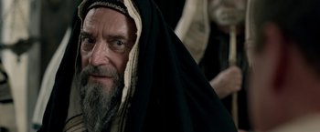 Movie still from “Risen” (2016), directed by Kevin Reynolds – An old man with a beard wearing a black robe; Close Up shot, Over the shoulder angle
