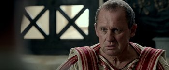 Movie still from “Risen” (2016), directed by Kevin Reynolds – An older man wearing a roman outfit looking at the camera; Close Up shot, Over the shoulder angle