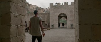 Movie still from “Risen” (2016), directed by Kevin Reynolds – A man holding a cell phone while standing in front of a gate; Wide shot, Over the shoulder angle