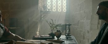 Movie still from “Risen” (2016), directed by Kevin Reynolds – A table in a room with a plant and a book; Wide shot, Low angle