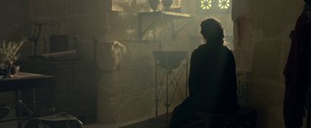 Movie still from “Risen” (2016), directed by Kevin Reynolds – A person sitting in a chair in front of a stone wall; Medium shot, Over the shoulder angle