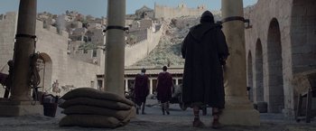 Movie still from “Risen” (2016), directed by Kevin Reynolds – A group of men in roman clothing walking in a courtyard; Extreme Wide shot, Low angle