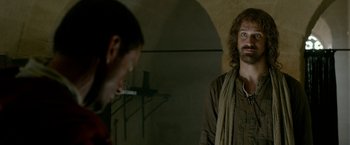 Movie still from “Risen” (2016), directed by Kevin Reynolds – A man standing next to another man in a dark room; Medium shot, Over the shoulder angle