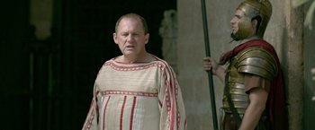 Movie still from “Risen” (2016), directed by Kevin Reynolds – A man wearing a red and white striped shirt and holding a spear; Medium shot, Over the shoulder angle