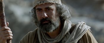 Movie still from “Risen” (2016), directed by Kevin Reynolds – A man with long hair and a beard wearing a hat; Close Up shot, Over the shoulder angle