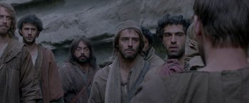 Movie still from “Risen” (2016), directed by Kevin Reynolds – A group of men standing next to each other in a cave; Medium shot, Over the shoulder angle