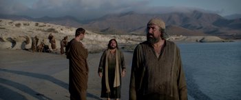 Movie still from “Risen” (2016), directed by Kevin Reynolds – A group of men standing next to each other on top of a beach; Medium shot, Low angle
