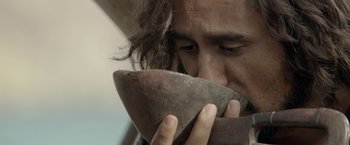 Movie still from “Risen” (2016), directed by Kevin Reynolds – A man with long hair is holding a wooden bowl; Extreme Close Up shot, High angle