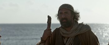Movie still from “Risen” (2016), directed by Kevin Reynolds – A man with a beard holding a wooden stick in front of the ocean; Close Up shot, Over the shoulder angle