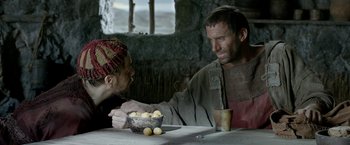 Movie still from “Risen” (2016), directed by Kevin Reynolds – A man sitting at a table with a bowl of fruit; Medium shot, Over the shoulder angle