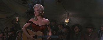 Movie still from “River of No Return” (1954), directed by Otto Preminger – A woman in a red and black dress holding a guitar; Medium shot, Low angle