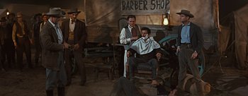 Movie still from “River of No Return” (1954), directed by Otto Preminger – A man sitting in front of another man while a man cuts another man's hair; Wide shot, Over the shoulder angle