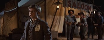 Movie still from “River of No Return” (1954), directed by Otto Preminger – A young boy wearing a name tag stands next to a man; Medium shot, Over the shoulder angle