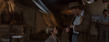 Movie still from “River of No Return” (1954), directed by Otto Preminger – A man and a boy are standing in front of a teepee; Medium shot, Over the shoulder angle