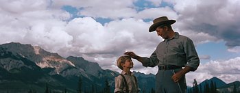 Movie still from “River of No Return” (1954), directed by Otto Preminger – A man in a cowboy hat is putting a hat on a boy's head; Medium shot, Low angle