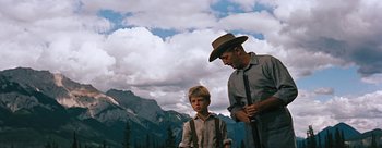 Movie still from “River of No Return” (1954), directed by Otto Preminger – A man and a young boy standing next to each other in front of mountains; Medium shot, Low angle