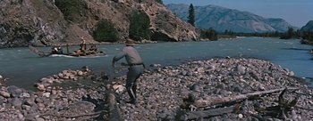 Movie still from “River of No Return” (1954), directed by Otto Preminger – A man standing on a rocky shore near a river; Wide shot, High angle