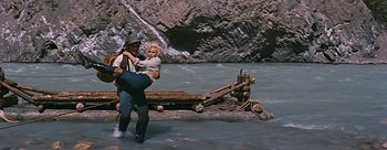 Movie still from “River of No Return” (1954), directed by Otto Preminger – A man carrying a woman across a body of water; Wide shot, High angle