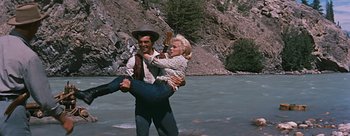 Movie still from “River of No Return” (1954), directed by Otto Preminger – A man holding a woman while standing on a river bank; Wide shot, Low angle