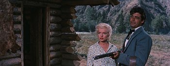 Movie still from “River of No Return” (1954), directed by Otto Preminger – A woman holding a gun while standing in front of a log cabin; Medium shot, Low angle