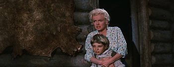 Movie still from “River of No Return” (1954), directed by Otto Preminger – An older woman holding a young boy next to a tree trunk; Medium shot, Low angle