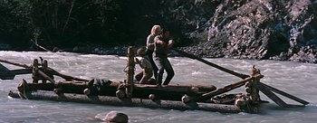 Movie still from “River of No Return” (1954), directed by Otto Preminger – A man and a woman crossing a river on a log raft; Wide shot, High angle