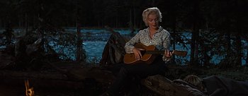 Movie still from “River of No Return” (1954), directed by Otto Preminger – A woman sitting on the ground playing a guitar; Wide shot, Low angle