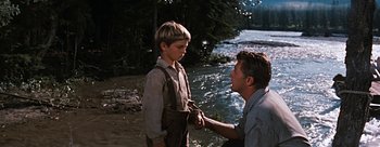 Movie still from “River of No Return” (1954), directed by Otto Preminger – A young boy and an older man standing next to a body of water; Medium shot, Over the shoulder angle