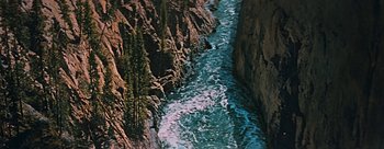 Movie still from “River of No Return” (1954), directed by Otto Preminger – A river running through a rocky area next to a forest; Extreme Wide shot, Overhead angle
