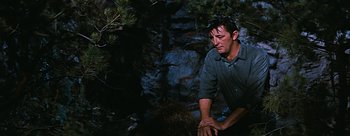 Movie still from “River of No Return” (1954), directed by Otto Preminger – A man sitting on the ground in front of a rock wall; Medium shot, Low angle