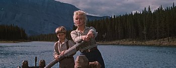 Movie still from “River of No Return” (1954), directed by Otto Preminger – A woman and a boy standing next to each other near a body of water; Medium shot, Low angle