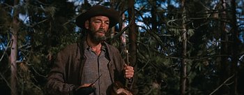 Movie still from “River of No Return” (1954), directed by Otto Preminger – A man in a hat holding a stick in the woods; Medium shot, Low angle