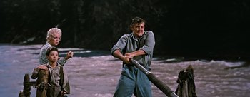 Movie still from “River of No Return” (1954), directed by Otto Preminger – A man holding a baseball bat while standing in the water; Medium shot, Low angle