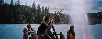Movie still from “River of No Return” (1954), directed by Otto Preminger – A man holding a gun while standing next to another man; Medium shot, Low angle
