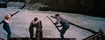 Movie still from “River of No Return” (1954), directed by Otto Preminger – A man holding two guns while standing next to another man holding a rifle; Wide shot, High angle