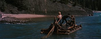 Movie still from “River of No Return” (1954), directed by Otto Preminger – A man and a woman standing on a raft in the water; Wide shot, High angle