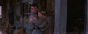 Movie still from “River of No Return” (1954), directed by Otto Preminger – A man and a boy are hugging outside a building; Medium shot, Low angle