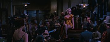 Movie still from “River of No Return” (1954), directed by Otto Preminger – A group of people sitting in a room with a guitar; Wide shot, Low angle