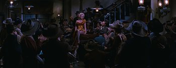 Movie still from “River of No Return” (1954), directed by Otto Preminger – A woman sitting on a chair in front of a crowd; Wide shot, Low angle