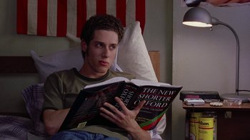 Movie still from “Road Trip” (2000), directed by Todd Phillips – A man reading a book in a bed room; Medium shot, High angle
