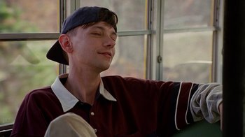Movie still from “Road Trip” (2000), directed by Todd Phillips – A young man wearing a baseball cap sitting in front of a window; Close Up shot, Low angle