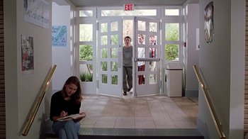 Movie still from “Road Trip” (2000), directed by Todd Phillips – A woman sitting in front of a door while a man stands in front of a door; Wide shot, High angle