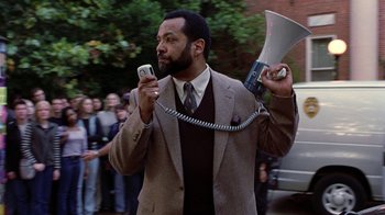 Movie still from “Road Trip” (2000), directed by Todd Phillips – A man in a suit holding a phone and a megaphone; Medium shot, Low angle