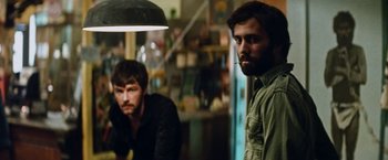 Movie still from “Road Games” (1981), directed by Richard Franklin – Two men standing next to each other in a room; Medium shot, Over the shoulder angle